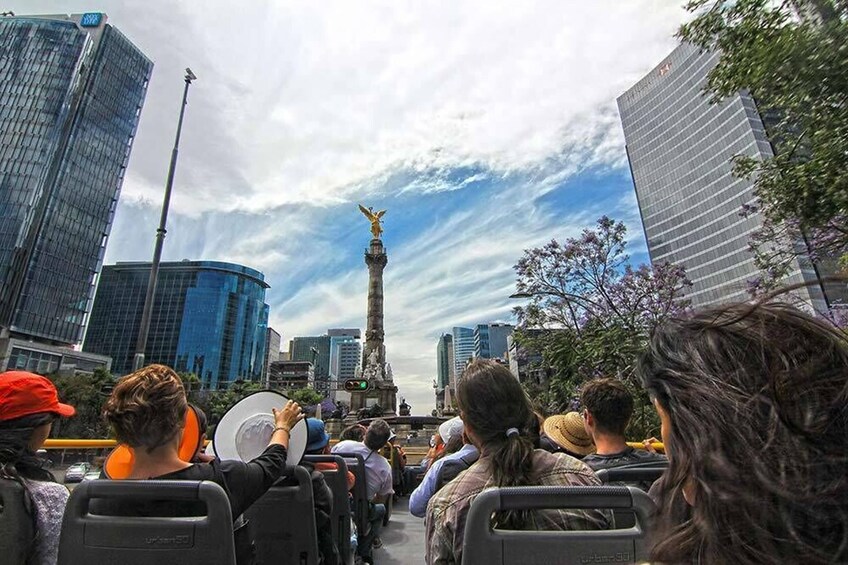 Un grupo de personas en un autobús observando un monumento alto con una estatua en la parte superior. 1