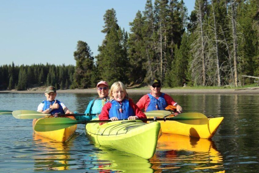 Quattro persone in kayak su un lago calmo, circondato da alberi. 1
