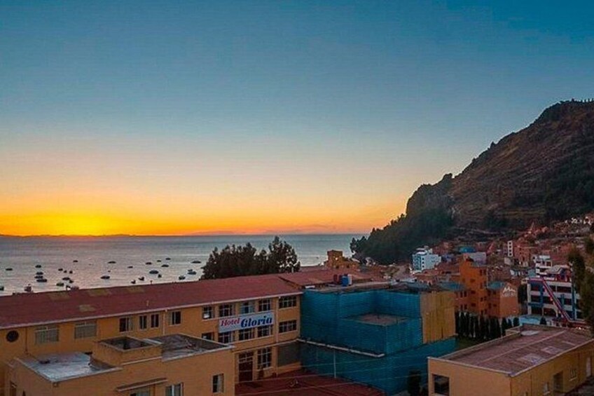 Un pueblo costero al atardecer con edificios, un hotel llamado 'Hotel Gloria' y barcos en el agua. 2