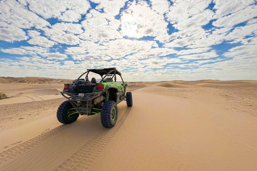 A green off-road vehicle driving on a sandy desert path. 1
