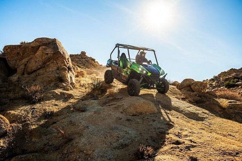 A green off-road vehicle on a rocky terrain with a clear sky. 2