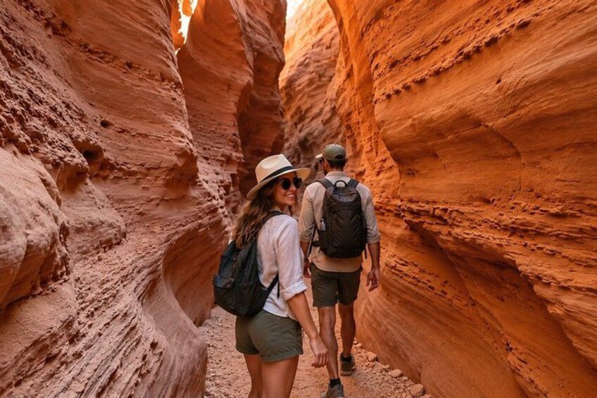 Two people hiking through a narrow canyon with reddish rock walls. 1