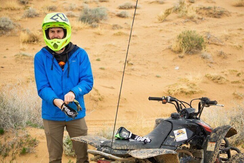 A person in a blue jacket and neon helmet standing next to a quad bike in a desert. 4