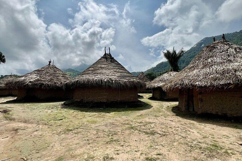 Thatched-roof huts in a rural setting with a dirt path and mountains in the background. 2