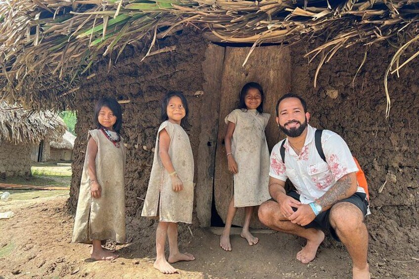 A rustic hut with a thatched roof, a dirt ground, and a person crouching in front. 1