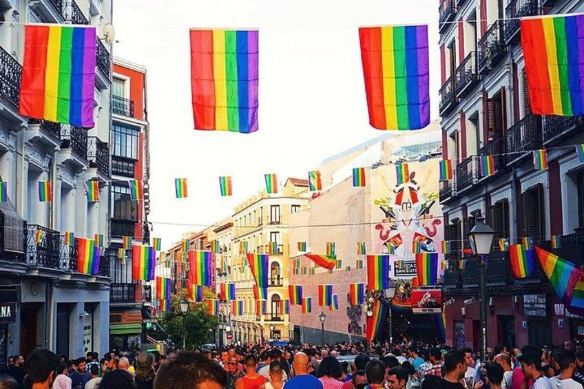 A crowded street with buildings and rainbow flags. 1