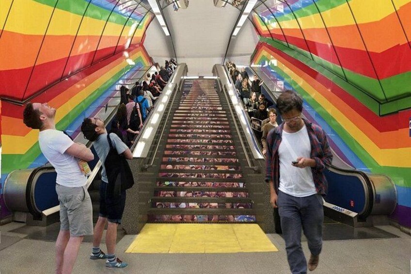 An escalator with rainbow-colored sides and people standing on it. 5