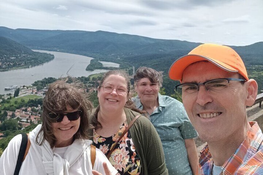 A group of people standing on a viewing platform overlooking a river and mountains. 1