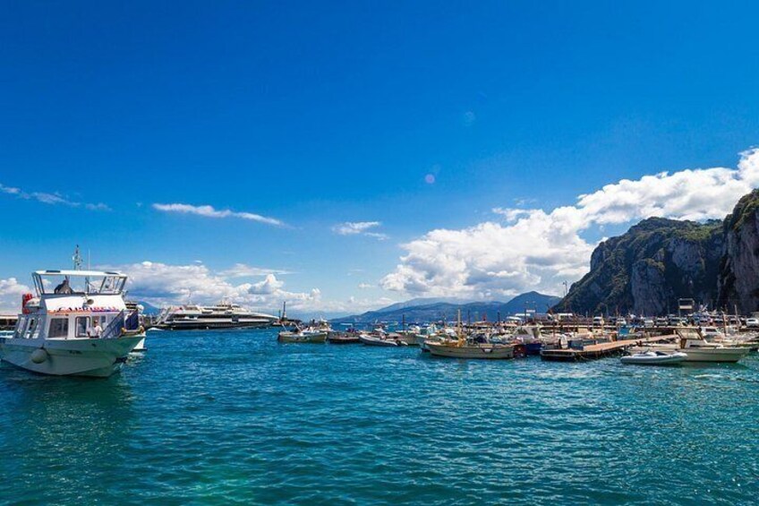 A coastal harbor with boats docked, a rocky cliff, and a clear blue sky. 1