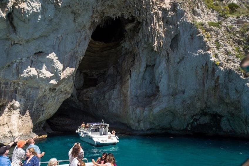 A boat navigating through a rocky cave entrance with clear blue water. 1