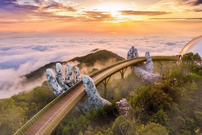 A bridge over a forested area with a hand sculpture and a sunset in the background. 1