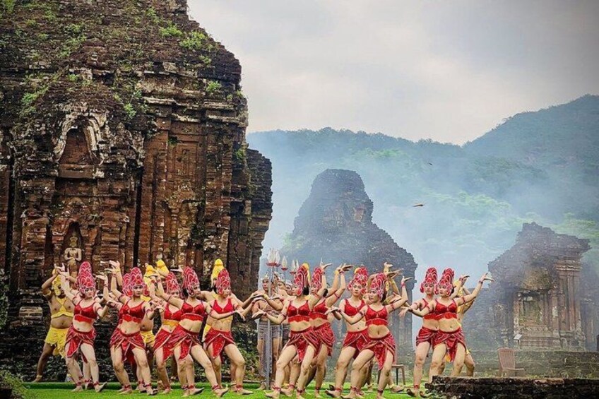 A group of dancers in red costumes performing in front of ancient ruins. 4