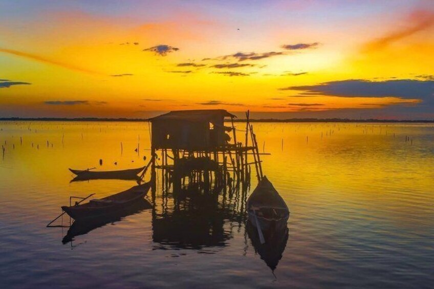 A wooden house on stilts, boats, and calm water at sunset. 3