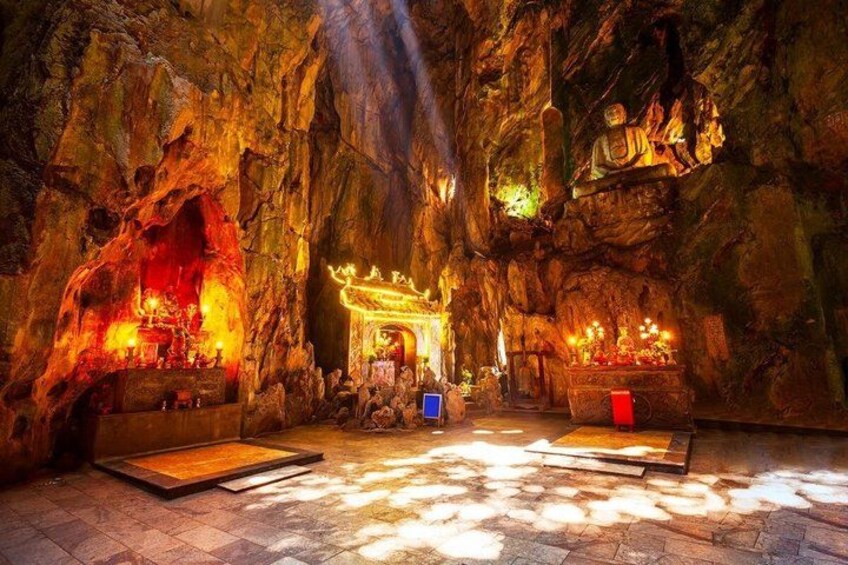 A cave interior with rock formations, a central altar, and a seating area. 2