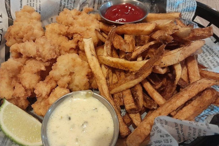 Una cesta con pescado frito dorado, papas fritas, un gajo de lima y dos salsas para mojar. 3
