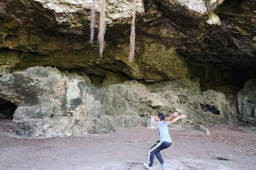 Una persona de pie en una cueva con paredes rocosas y raíces colgantes. 4