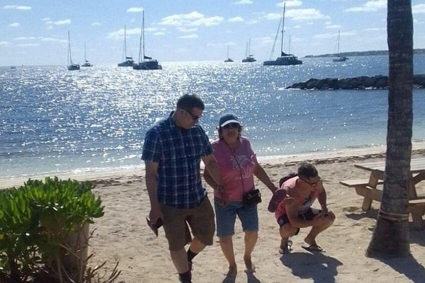 Una playa con gente caminando, una palmera y veleros al fondo. 2