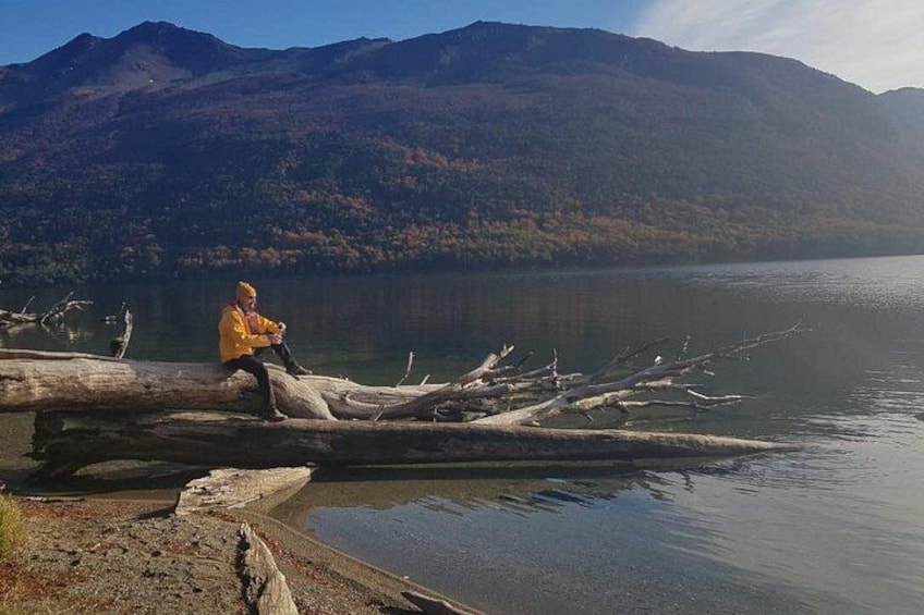 A person sitting on a log by a calm lake with mountains in the background. 2