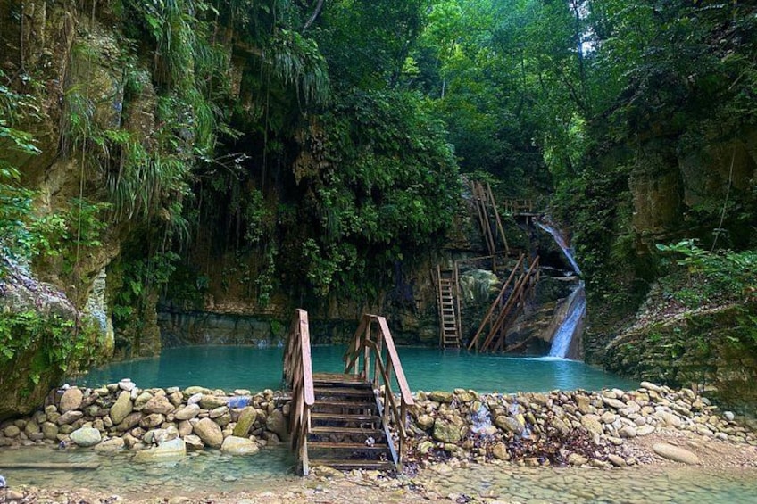 A natural pool with a wooden bridge, surrounded by lush greenery and a waterfall. 3