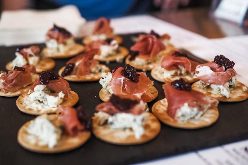 A tray of appetizers with prosciutto, cheese, and berries on crackers. 3