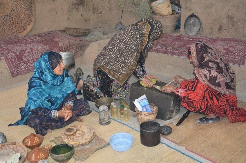 Three women sitting on the floor in a traditional setting with pottery and textiles. 1