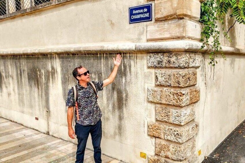 A person standing next to a wall with a sign reading 'Avenue de Champagne'. 3