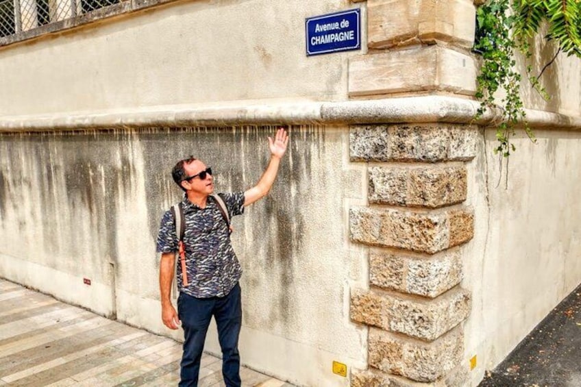 Ein Mann steht an einer Wand mit einem Schild, auf dem 'Avenue de Champagne' steht. 4