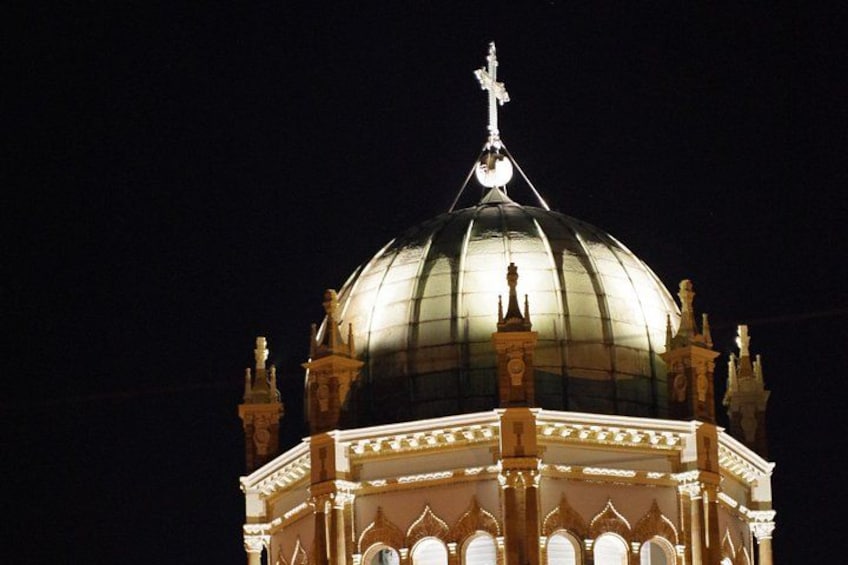 Una cúpula grande e iluminada con una cruz en la parte superior, rodeada de detalles arquitectónicos ornamentales. 2