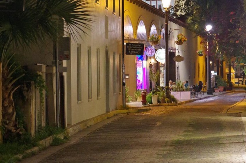 Una calle nocturna con un edificio que tiene ventanas arqueadas y plantas colgantes. 4