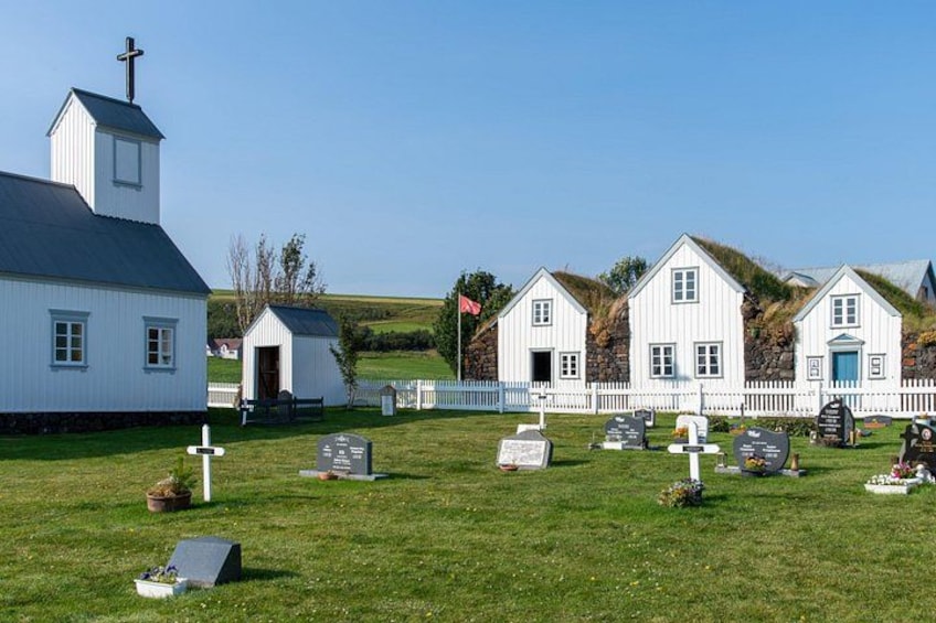 A white church with a steeple, a white fence, and several gravestones in a grassy field. 2
