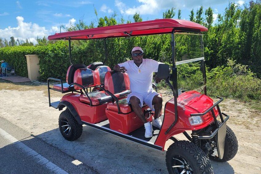 A man in a white outfit sitting in a red golf cart on a paved road. 2