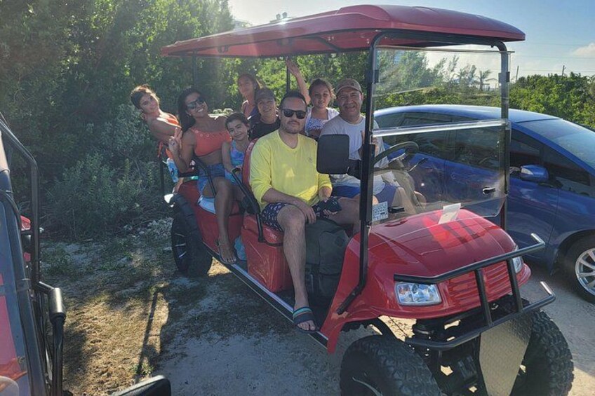 A red golf cart with passengers, parked on a dirt path with a blue car in the background. 4