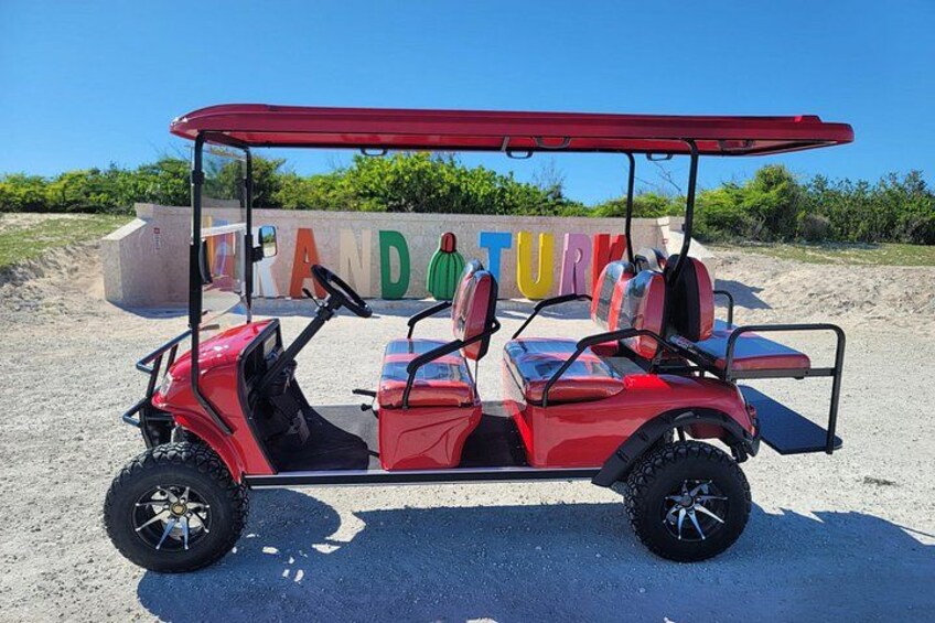 A red golf cart parked on a sandy area with a sign in the background. 1