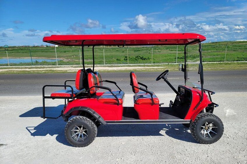 A red golf cart parked on a gravel surface with a clear sky and green landscape in the background. 3
