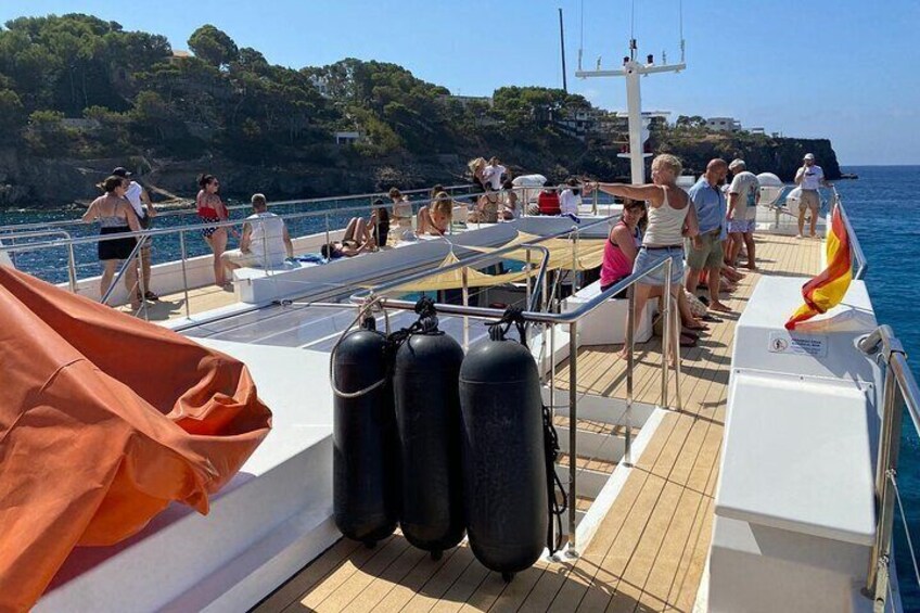 A boat deck with people, a flag, and a rocky coastline in the background. 2