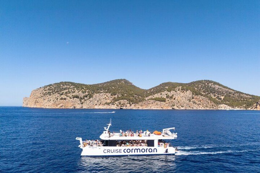 A white cruise ship named 'CRUISE CORMORAN' sailing in the sea with rocky hills in the background. 3