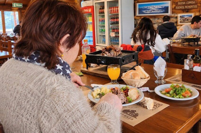 Une personne est assise à une table de restaurant, où se trouvent divers plats, notamment un panier de pain, une assiette de salade et un verre de jus d’orange. 5