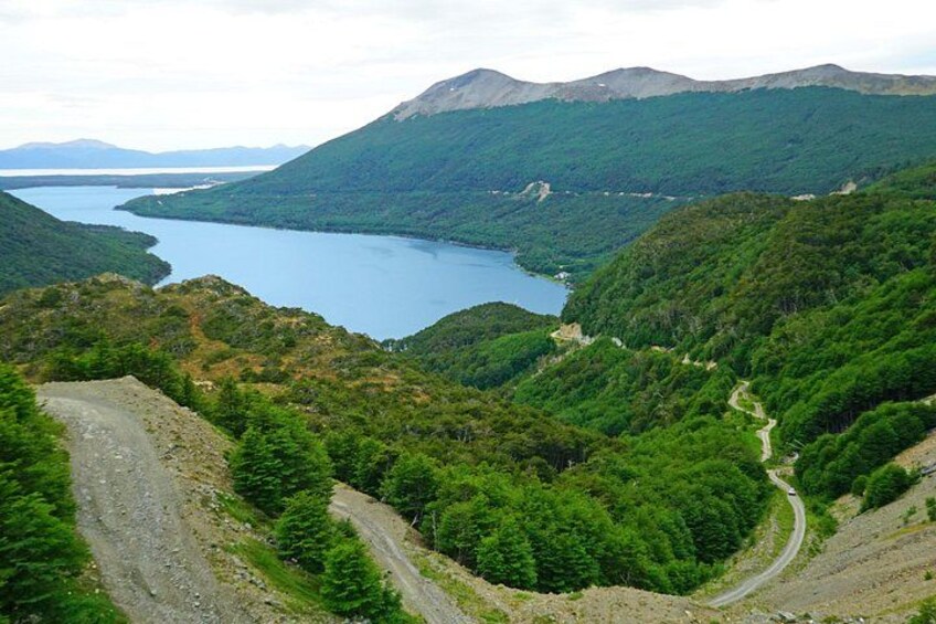 Een bergachtig landschap met een kronkelende weg, dicht bos en een meer. 1