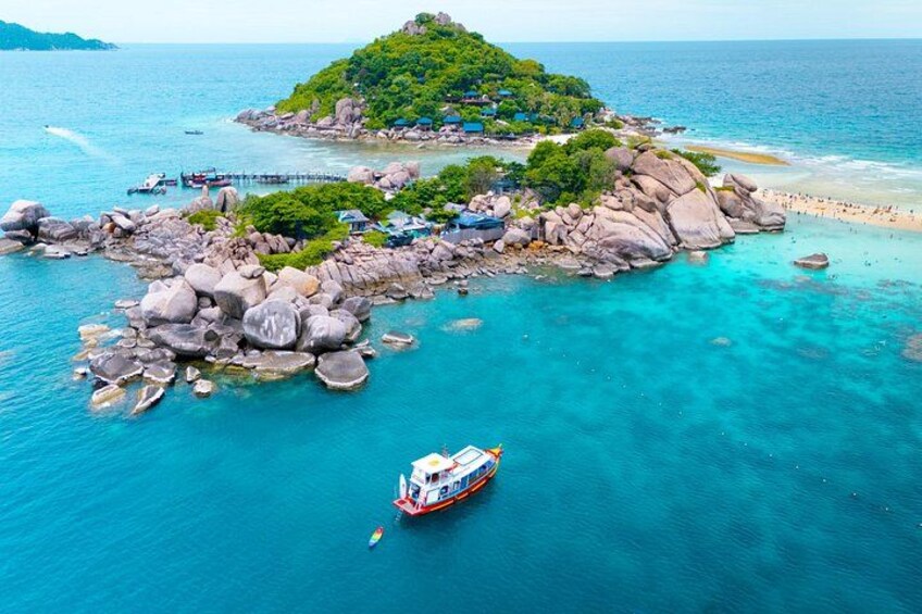 A tropical island with clear turquoise waters, a boat, and a rocky shoreline. 1