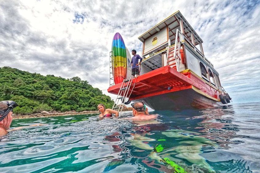A boat with a colorful rocket-like structure, people swimming, and a forested shoreline. 2