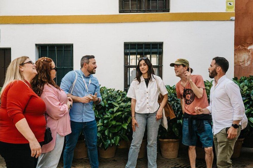 A group of people standing in a courtyard with potted plants and a building with windows in the background. 3