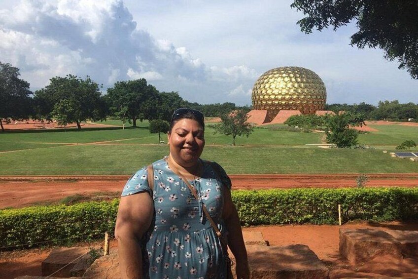 A person standing in front of a large golden sphere structure, likely a famous landmark, with green grass and trees in the background. 5
