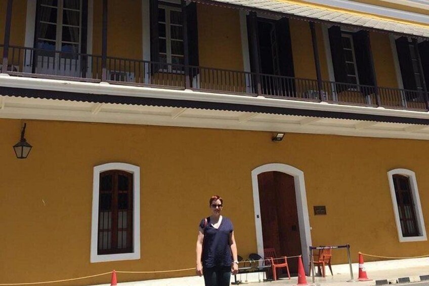 A person standing in front of a yellow building with arched windows and a balcony. 3