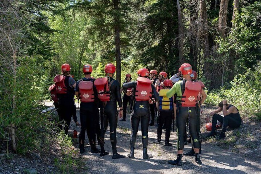 A group of people in red helmets and life vests standing in a forested area. 1