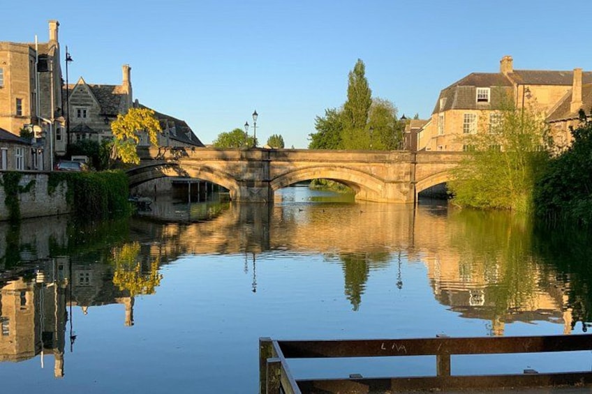 A stone bridge over a calm river, surrounded by buildings and trees. 1