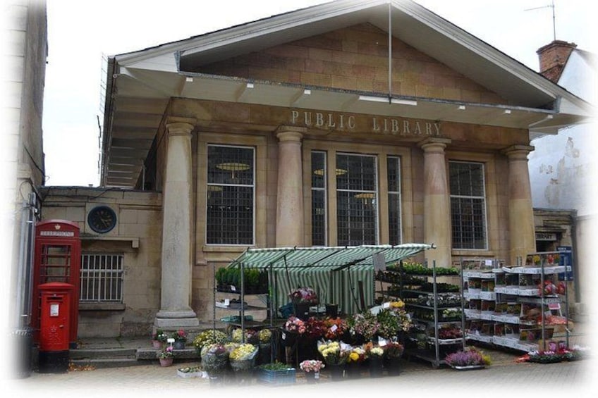 A public library with a classic facade, a red telephone booth, and a flower stall in front. 4