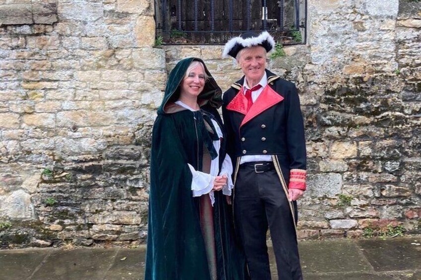 Two people in historical costumes standing in front of a stone building. 2