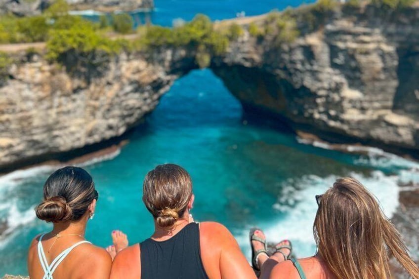 Three people overlooking a coastal landscape with a prominent rock formation and clear blue waters. 3