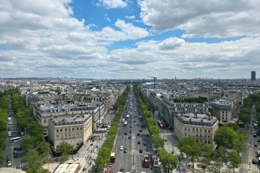 A cityscape with a wide street flanked by buildings, a clear sky, and distant city skyline. 3