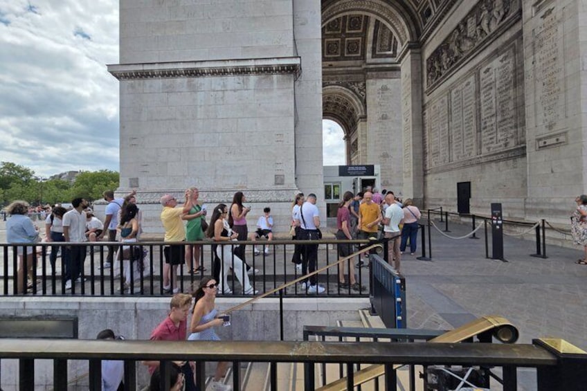 A large stone monument with inscriptions, a crowd of people, and a metal railing. 5
